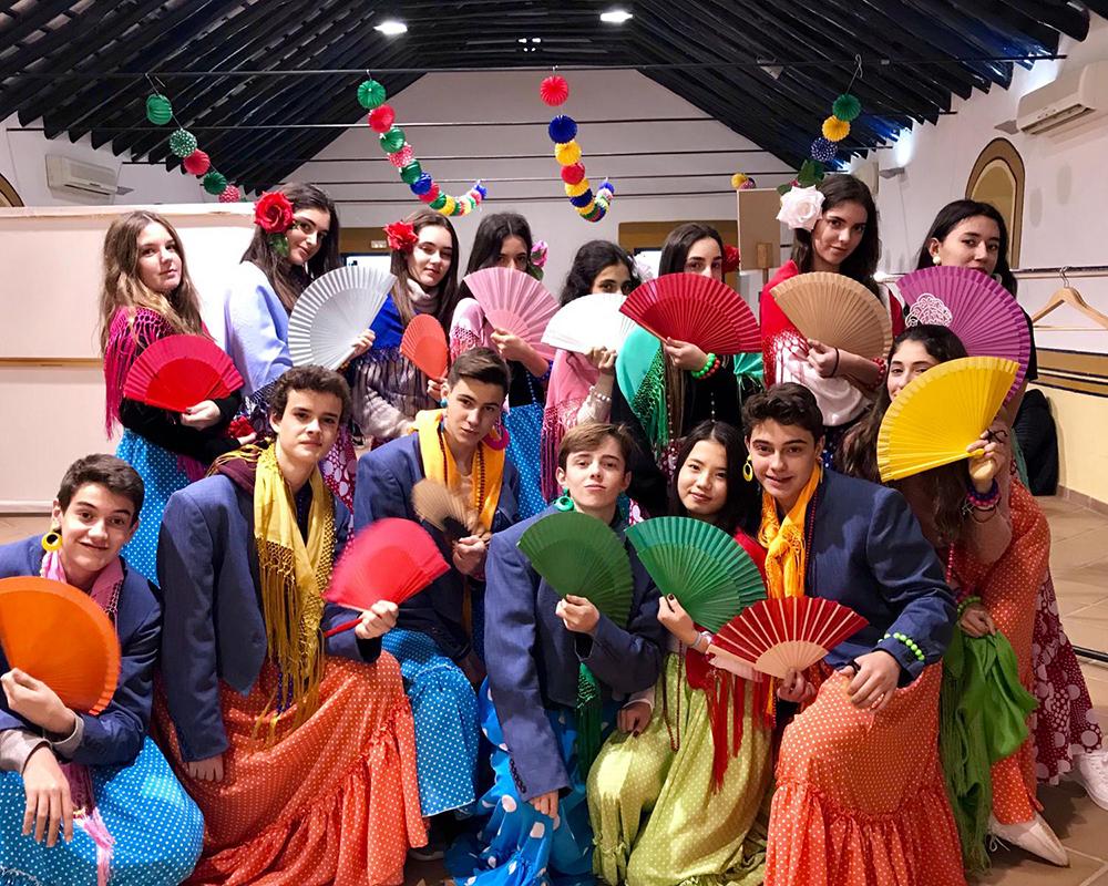 一群学生穿着五颜六色的弗拉门戈服装，手持扇子, 庆祝西班牙文化, 在有装饰的室内环境中, 展示文化多样性和参与性.